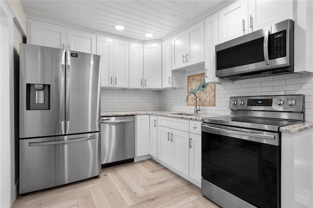 kitchen with light stone countertops, white cabinetry, sink, stainless steel appliances, and light parquet floors