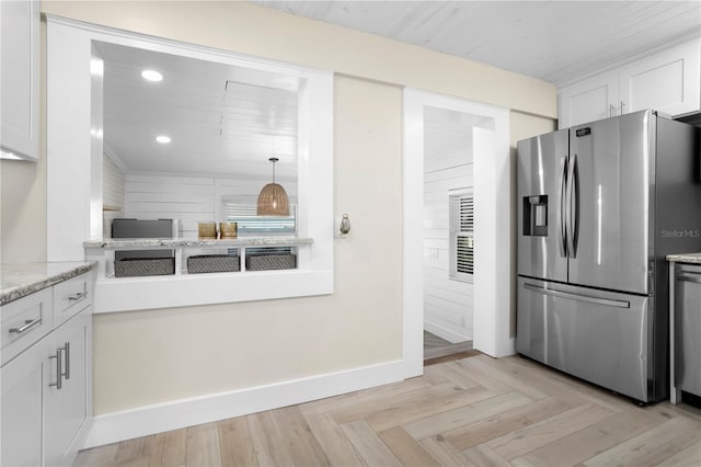 kitchen with white cabinets, stainless steel fridge, light stone countertops, and light parquet flooring