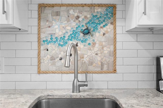 interior details featuring white cabinetry, light stone countertops, and sink