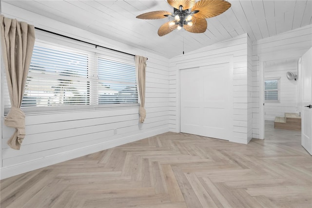 unfurnished bedroom with ceiling fan, a closet, light parquet floors, and wooden walls