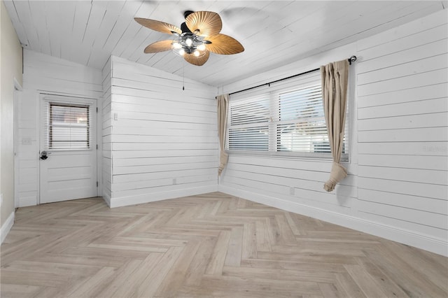 spare room featuring ceiling fan, wood walls, light parquet floors, and vaulted ceiling