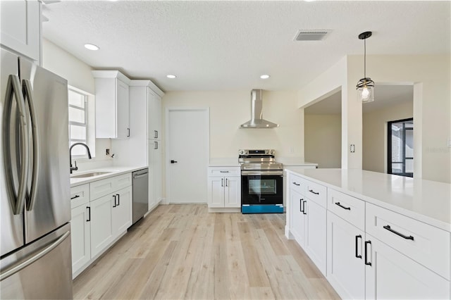 kitchen featuring wall chimney exhaust hood, stainless steel appliances, sink, decorative light fixtures, and white cabinetry