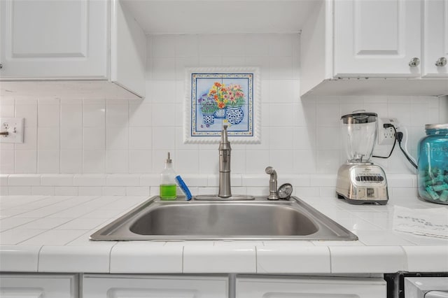 kitchen featuring a sink, tasteful backsplash, tile counters, and white cabinets