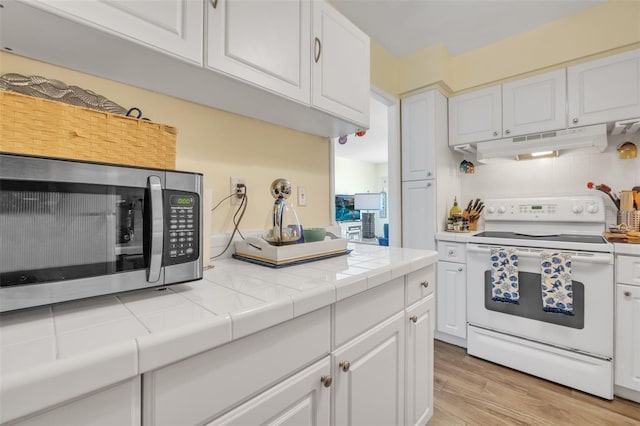 kitchen with electric range, under cabinet range hood, stainless steel microwave, white cabinets, and decorative backsplash