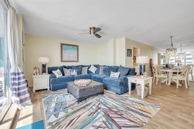 living room with light wood-type flooring and ceiling fan with notable chandelier