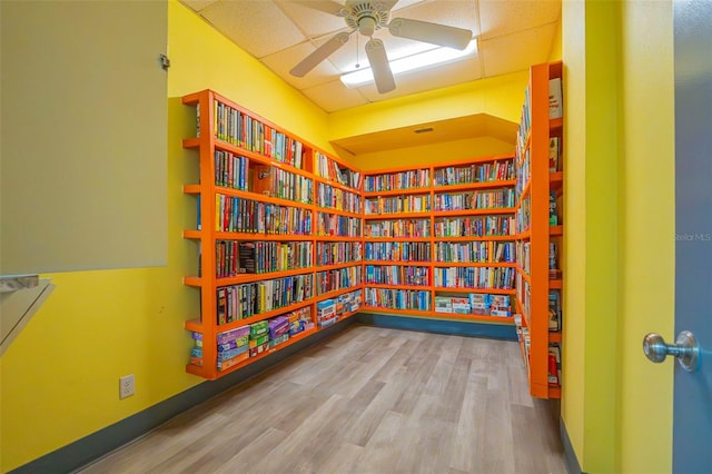 interior space with ceiling fan, a drop ceiling, baseboards, and wood finished floors