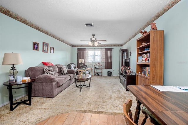 living room with ceiling fan, light wood-type flooring, and a textured ceiling