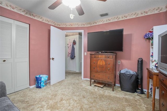 bedroom with ceiling fan, a closet, light colored carpet, and a textured ceiling