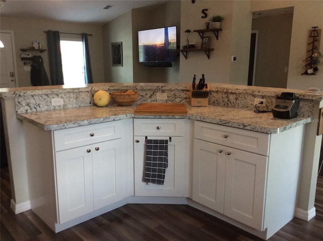 kitchen featuring kitchen peninsula, light stone counters, white cabinets, and dark hardwood / wood-style floors