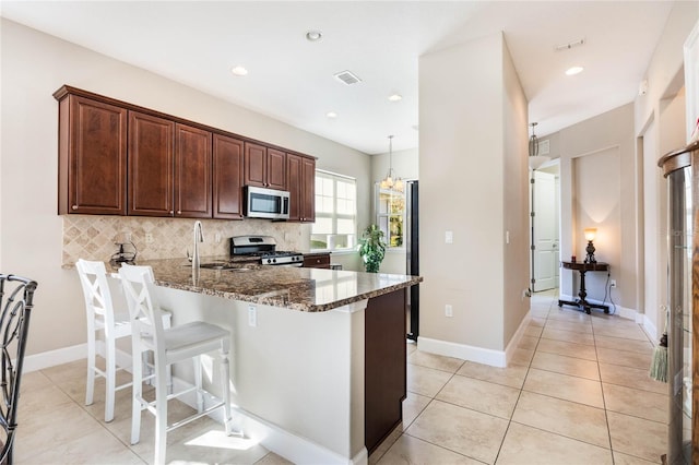 kitchen with pendant lighting, dark stone counters, a kitchen bar, decorative backsplash, and appliances with stainless steel finishes