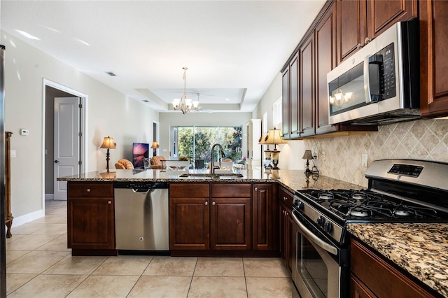 kitchen featuring kitchen peninsula, appliances with stainless steel finishes, a raised ceiling, sink, and a chandelier