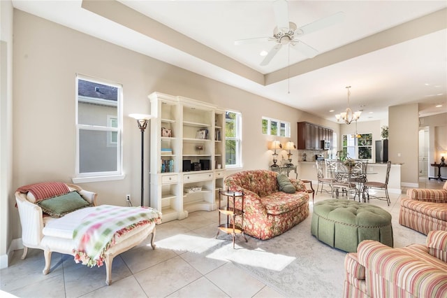 living room with ceiling fan with notable chandelier, light tile patterned flooring, and a tray ceiling