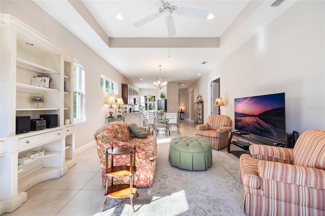 living room with ceiling fan with notable chandelier, light tile patterned floors, built in shelves, and a tray ceiling