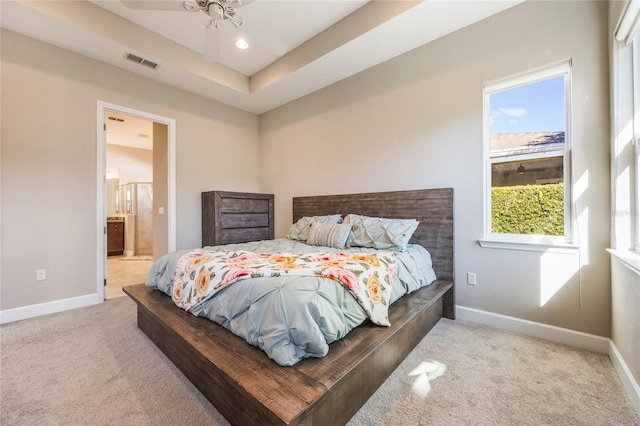 carpeted bedroom featuring a tray ceiling, ensuite bath, and ceiling fan