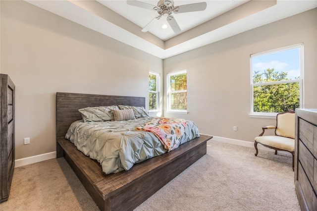 bedroom with light carpet, multiple windows, a tray ceiling, and ceiling fan