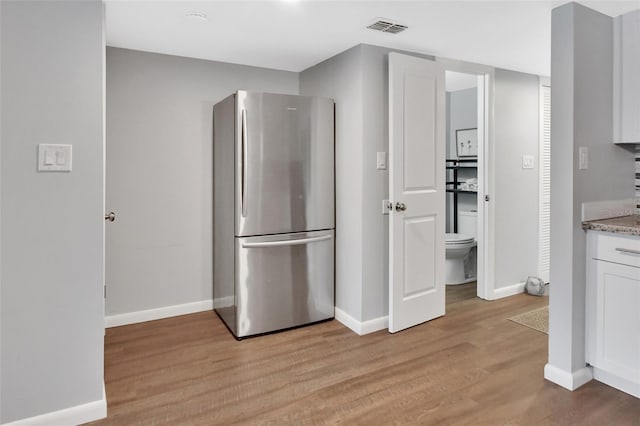 kitchen with stainless steel fridge, white cabinets, light stone counters, and light wood-type flooring