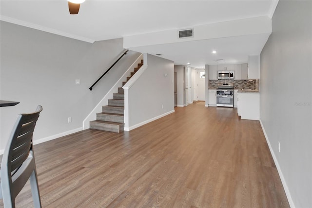 unfurnished living room featuring light wood-type flooring, ceiling fan, crown molding, and sink