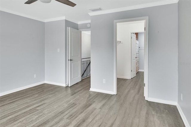 interior space with a walk in closet, light hardwood / wood-style flooring, ceiling fan, and crown molding