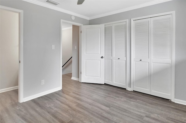 unfurnished bedroom with ceiling fan, crown molding, two closets, and light wood-type flooring