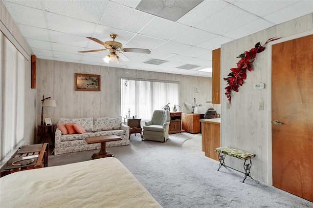 living room featuring a paneled ceiling, ceiling fan, light colored carpet, and wooden walls