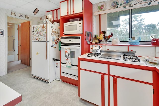 kitchen featuring white appliances, a drop ceiling, and white cabinetry