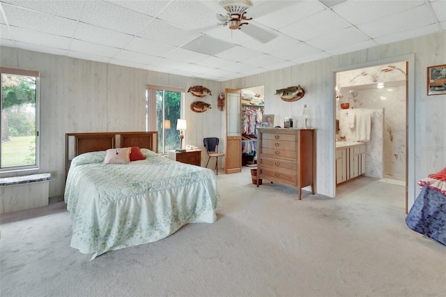 bedroom featuring ensuite bath, a walk in closet, a closet, light colored carpet, and ceiling fan