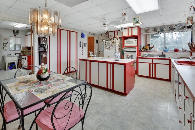 kitchen with white appliances, hanging light fixtures, sink, a kitchen island, and a paneled ceiling