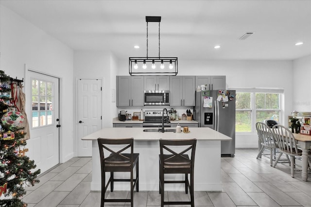 kitchen with a center island with sink, a kitchen breakfast bar, hanging light fixtures, gray cabinets, and appliances with stainless steel finishes