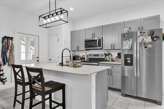 kitchen featuring hanging light fixtures, an island with sink, a breakfast bar area, gray cabinets, and appliances with stainless steel finishes