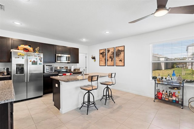 kitchen with a breakfast bar, stone countertops, stainless steel appliances, and a kitchen island with sink