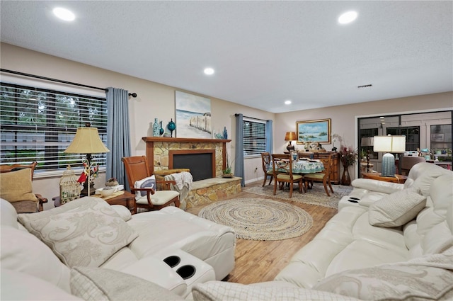 living room featuring hardwood / wood-style flooring, a stone fireplace, and a textured ceiling