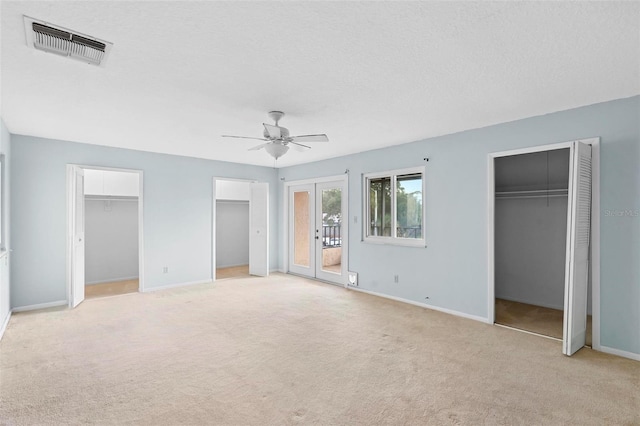 unfurnished bedroom featuring french doors, ceiling fan, a textured ceiling, light colored carpet, and multiple closets