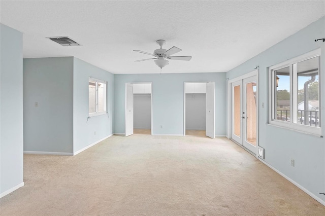 empty room featuring ceiling fan, french doors, light colored carpet, and a textured ceiling