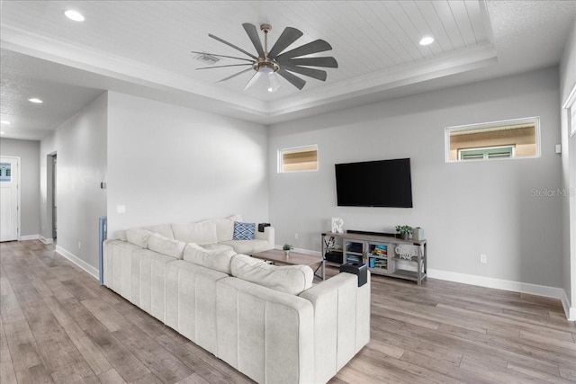 living room with ornamental molding, a tray ceiling, ceiling fan, and light hardwood / wood-style floors