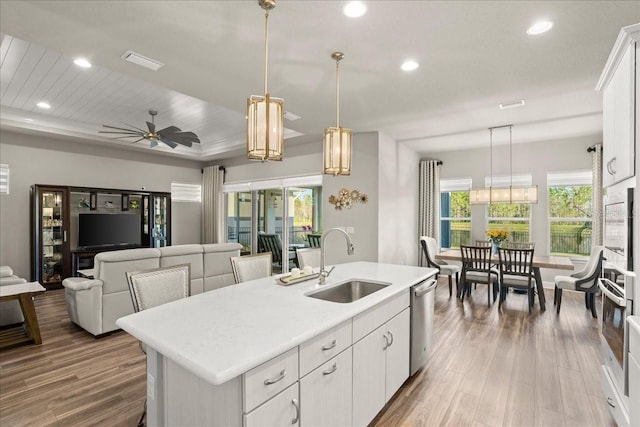 kitchen featuring ceiling fan, sink, decorative light fixtures, a center island with sink, and white cabinets