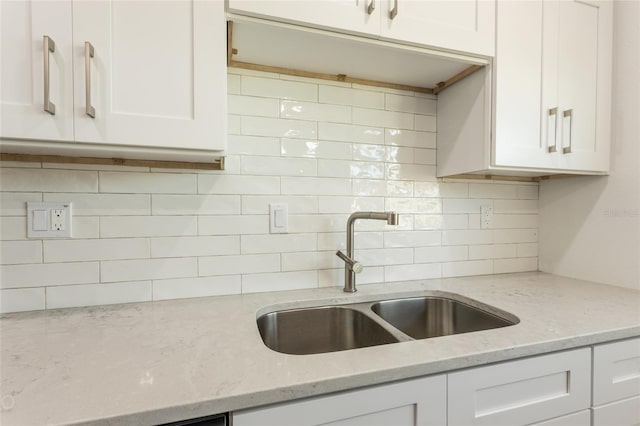 kitchen featuring white cabinets, decorative backsplash, light stone counters, and sink