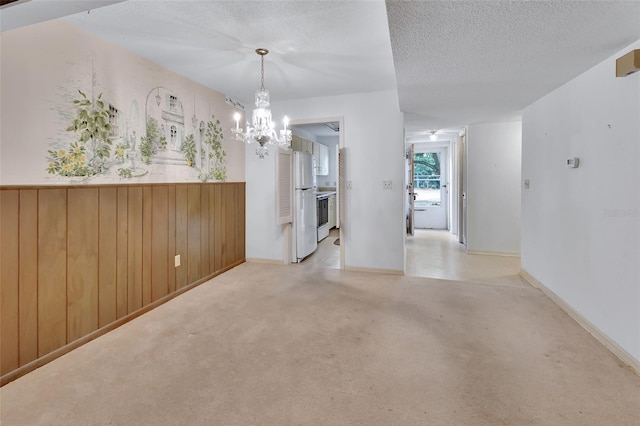 unfurnished room with a textured ceiling, a notable chandelier, and wood walls