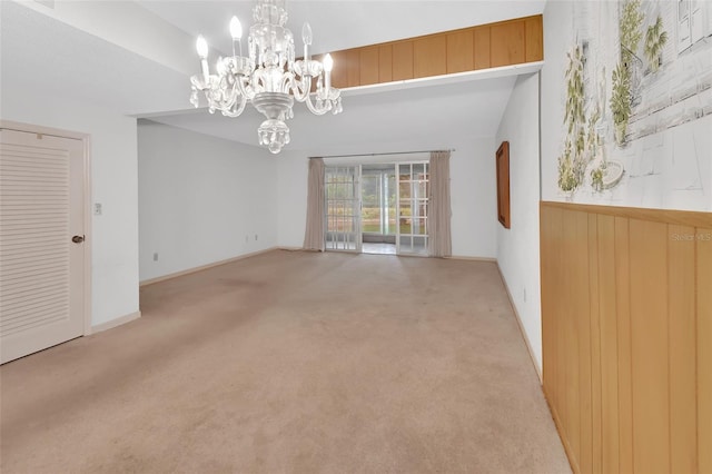 carpeted spare room with wood walls, vaulted ceiling, and a notable chandelier