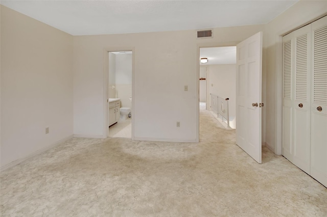 unfurnished bedroom featuring light carpet, ensuite bathroom, and a closet