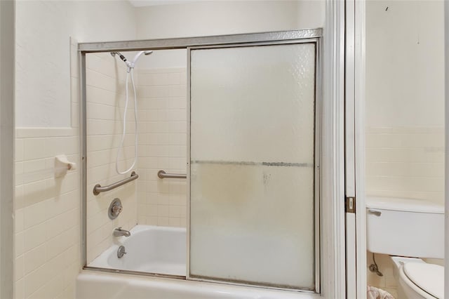 bathroom featuring shower / bath combination with glass door, toilet, and tile walls