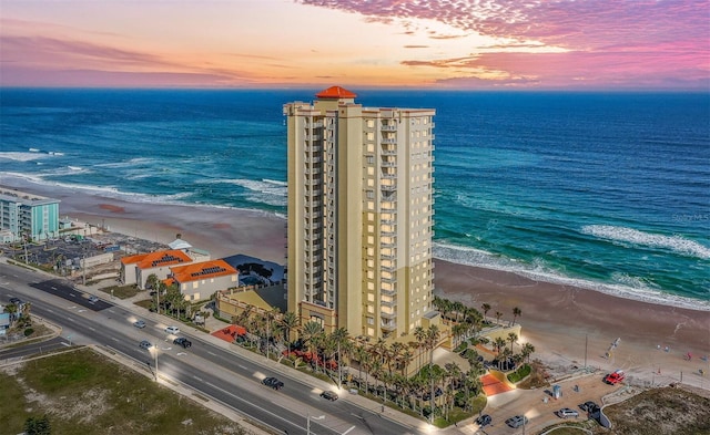 aerial view at dusk with a water view and a view of the beach