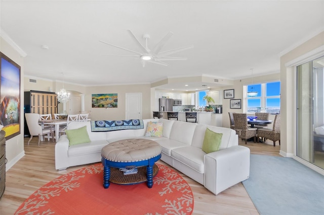 living room with ceiling fan with notable chandelier, light wood-type flooring, and ornamental molding