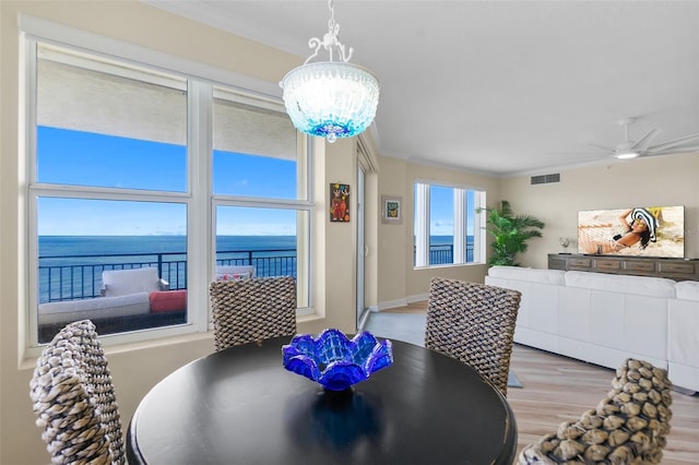 dining room with light wood-type flooring, ceiling fan with notable chandelier, a water view, and crown molding