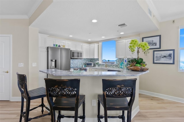 kitchen featuring backsplash, white cabinets, a kitchen breakfast bar, sink, and appliances with stainless steel finishes