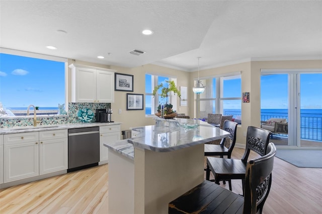 kitchen with dishwasher, a center island, hanging light fixtures, white cabinets, and a water view