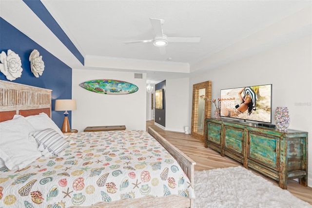 bedroom with a tray ceiling, ceiling fan, crown molding, and light wood-type flooring