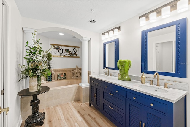 bathroom featuring hardwood / wood-style floors, vanity, a relaxing tiled tub, and decorative columns