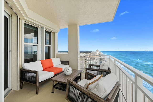 balcony with an outdoor living space, a water view, and a view of the beach