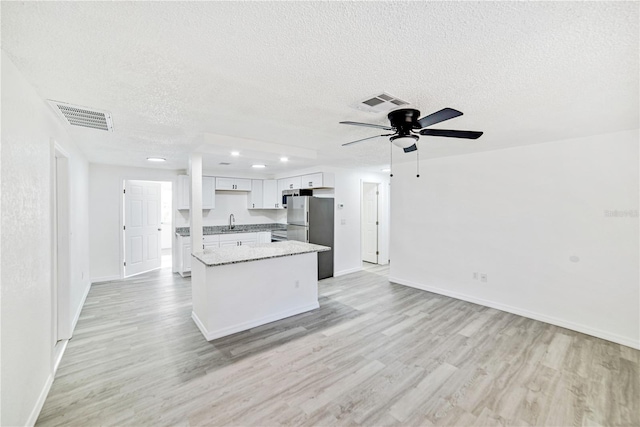 kitchen featuring stainless steel refrigerator, sink, light hardwood / wood-style flooring, a textured ceiling, and white cabinets