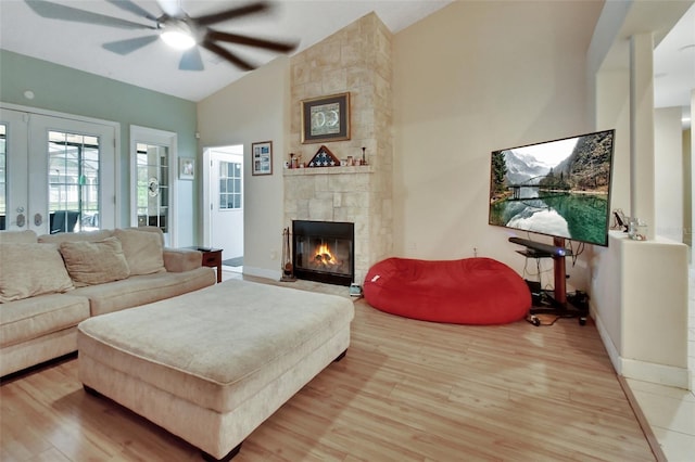 living room featuring hardwood / wood-style floors, ceiling fan, a stone fireplace, and vaulted ceiling